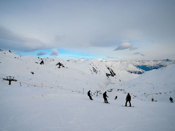 Silhouette people skiing on ski slope against cloudy sky