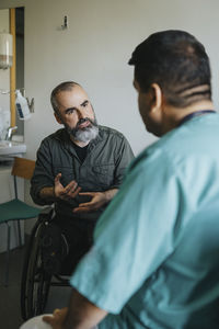 Mature patient in wheelchair explaining doctor in clinic