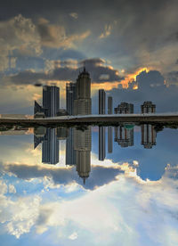 Reflection of buildings in city against sky during sunset