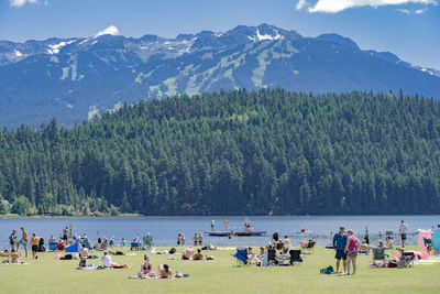 People on field by lake against mountains