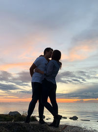 Full length of friends standing on beach against sky during sunset