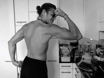 Shirtless man flexing muscles in kitchen at home