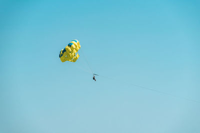 Low angle view of people paragliding against clear blue sky