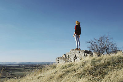 Full length of woman standing on rock against blue sky