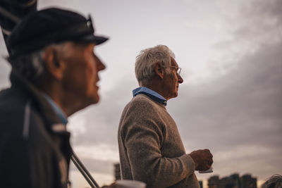 Male friends with coffee cup looking away against sky during sunset