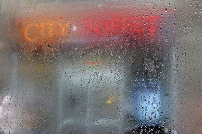 Illuminated text seen through wet glass window of bus