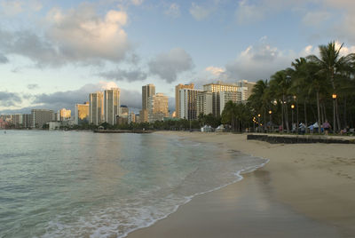 Sea by buildings against cloudy sky