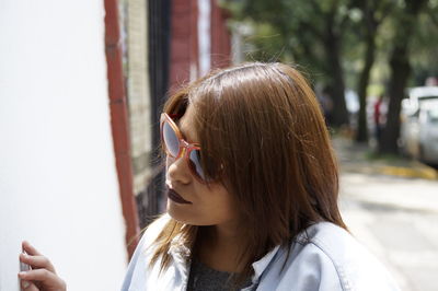 Close-up of woman in sunglasses looking away by wall