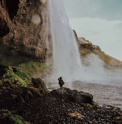 Woman standing on rock against waterfall