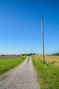 Road amidst field against clear blue sky