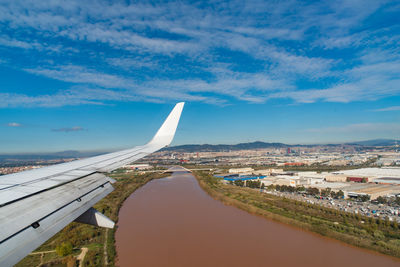 Cropped image of airplane wing overlooking cityscape against cloudy sky