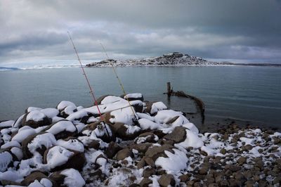 Snow covered land by sea against sky