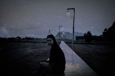 Portrait of woman sitting against sky at night