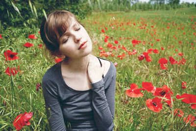 Woman with eyes closed sitting amidst flowering plants on field