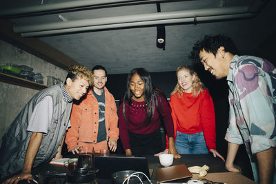 Smiling entrepreneurs looking at laptop while standing by table in creative office