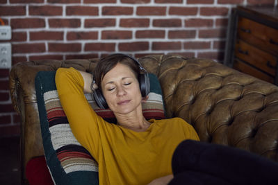 Woman with headphone lying on sofa, listening music