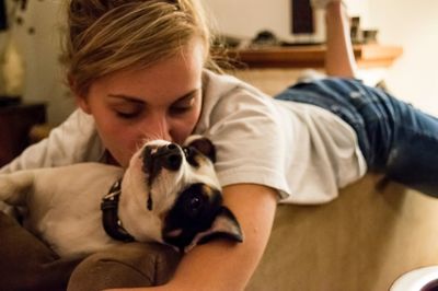 Young woman kissing puppy while lying on sofa at home