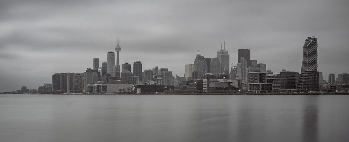 Sea by modern buildings against sky in city