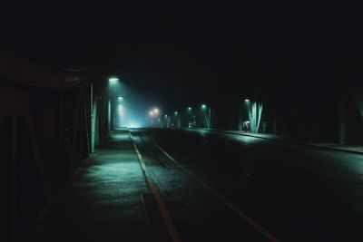 Empty road along illuminated street lights at night