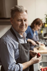 Portrait of mature man holding strawberry with woman in background