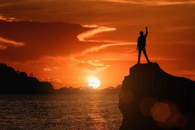 Silhouette man standing on rock against sea during sunset