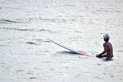 Rear view of shirtless man with surfboard in sea