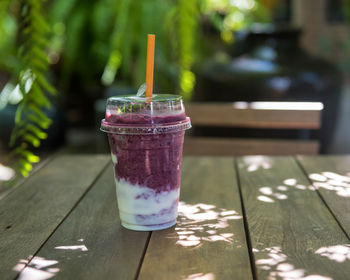 Blueberry yogurt smooties on wooden table of coffee shop garden cafe with blur foliage light