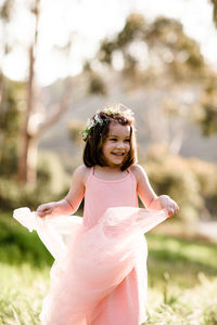 Young girl in tutu and flower crown standing in field, smiling