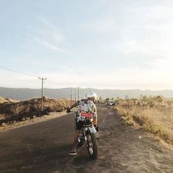 Rear view of man riding motorcycle on road against sky