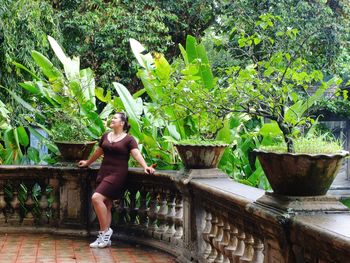 Full length of smiling woman looking up while standing by potted plants