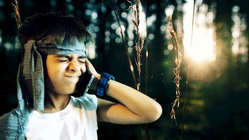 Boy talking on mobile phone while making face at forest