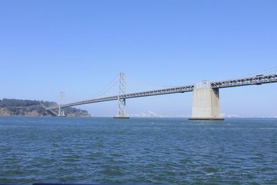 Suspension bridge over river against clear blue sky