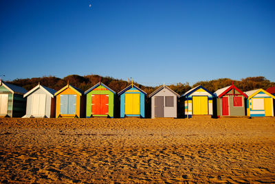 Beach huts by buildings against clear blue sky