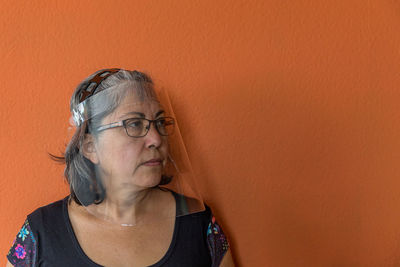 Side view portrait of mature woman standing on orange background, glasses wearing face shield