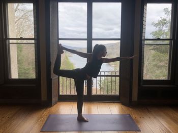 Full length of woman exercising against lake seen through window