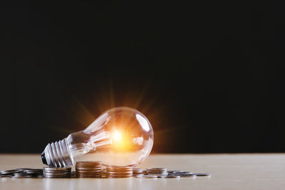 Close-up of illuminated light bulb on table against black background