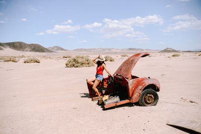 Full length of woman sitting on abandoned vehicle at desert