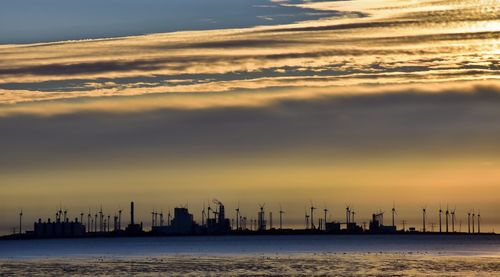 Windmills at beach against sky during sunset