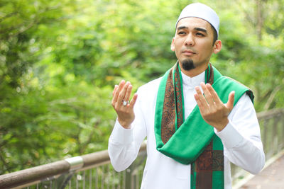 Mid adult man praying while standing by railing at park