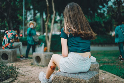 Rear view of women sitting on land by trees in forest