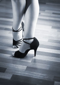 Low section of woman wearing high heels standing on hardwood floor