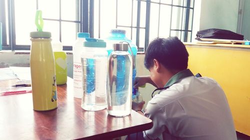 Man holding bottle on table by window