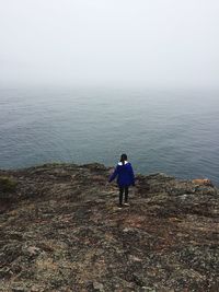 Rear view of woman walking on cliff against sea and sky