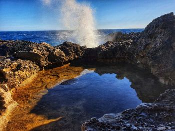 Sea waves splashing on rock against sky