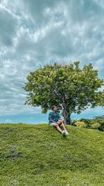 Rear view of man sitting on field against sky