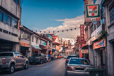 Cars on street by buildings in city against sky