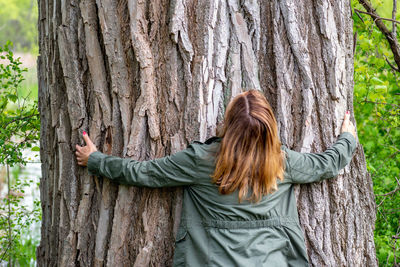 Rear view of woman hugging tree in forest