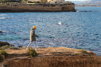 Young man walking on cliff against sea