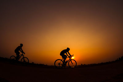 Silhouette friends riding bicycle against sky during sunset