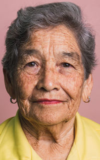 Elderly female with short gray hair and brown eyes looking at camera on pink background in studio